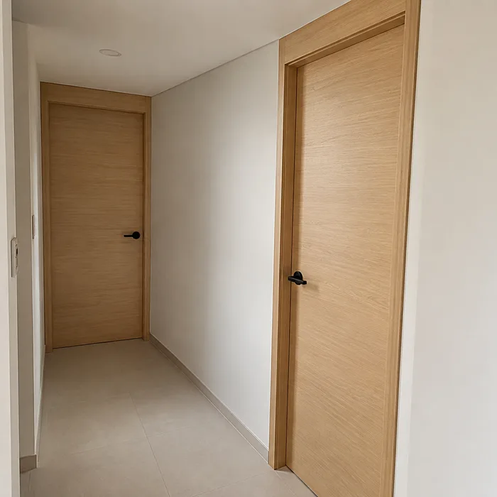 Pasillo moderno con puertas de madera clara y paredes blancas en Bucaramanga