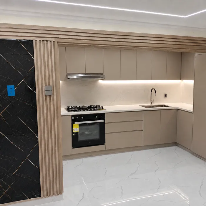 Cocina integral beige con encimera blanca, estufa negra y piso mármol en Bucaramanga